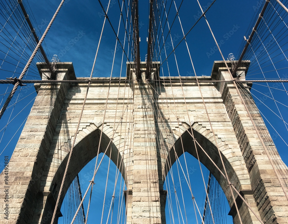 Naklejka premium Detalles arquitectónicos del famoso puente de Brooklyn en New York, USA. Cableado y arcos de piedra vistos desde abajo, desde el paso peatonal, en uno de sus dos pilares, el más cercano a Manhattan.