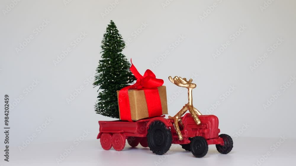 Red toy tractor features gift box with red ribbon and bow, Christmas tree in trailer, reindeer at the wheel, captured in a 360-degree spin video. Red toy tractor features gift box with red ribbon and bow, Christmas tree in trailer, reindeer at the wheel, captured in a 360-degree spin video.