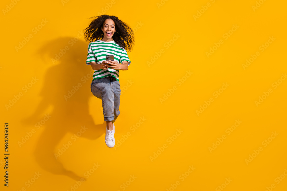 Full body portrait of nice young girl use phone jump run wear striped t-shirt isolated on yellow color background Full body portrait of nice young girl use phone jump run wear striped t-shirt isolated on yellow color background