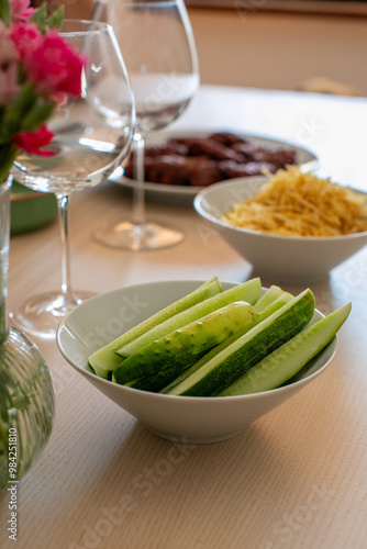 A festive table is set with fresh cucumber slices, snacks, and wine glasses, perfect for a summer gathering or healthy eating concept