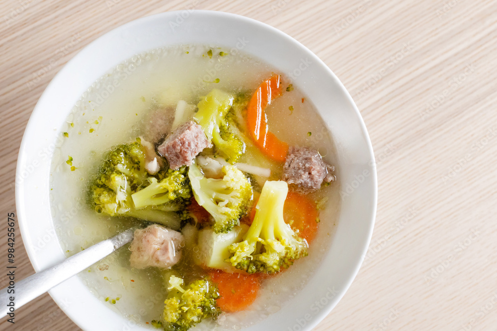 A bowl of nutritious homemade vegetable and meatball soup on a wooden table, perfect for comforting winter meals A bowl of nutritious homemade vegetable and meatball soup on a wooden table, perfect for comforting winter meals