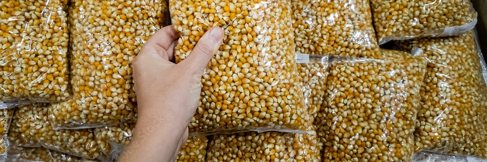 A hand holds a sealed bag of popcorn kernels among a large stack, symbolizing food storage and preparation A hand holds a sealed bag of popcorn kernels among a large stack, symbolizing food storage and preparation
