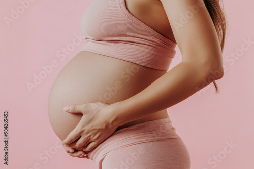 Close up side view of pregnant young expecting woman round belly pink background. Maternity concept