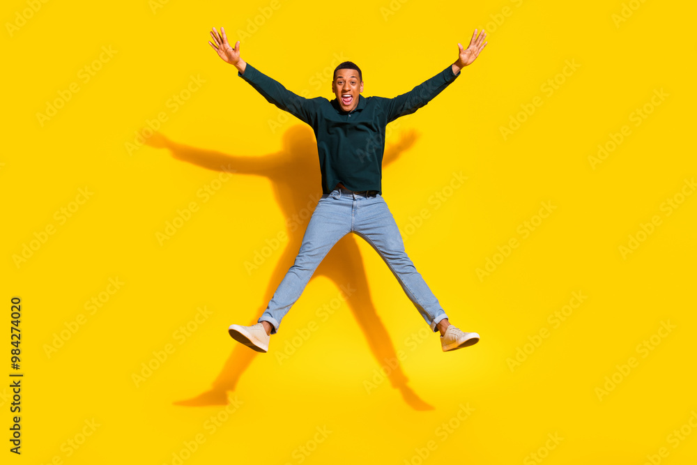 Fototapeta premium Full length photo of attractive young man jump star pose spread arms legs dressed stylish green clothes isolated on yellow color background