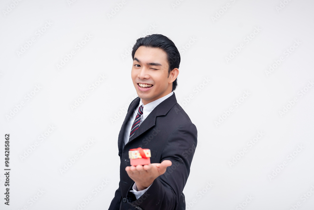 A young and kind asian business executive winking while handing over a very small gift on the palm of his hand. A token of appreciation. Isolated on a white background. A young and kind asian business executive winking while handing over a very small gift on the palm of his hand. A token of appreciation. Isolated on a white background.