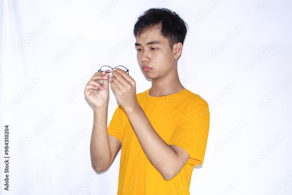 an asian teenager wearing a yellow shirt and glasses, is checking his glasses carefully an asian teenager wearing a yellow shirt and glasses, is checking his glasses carefully