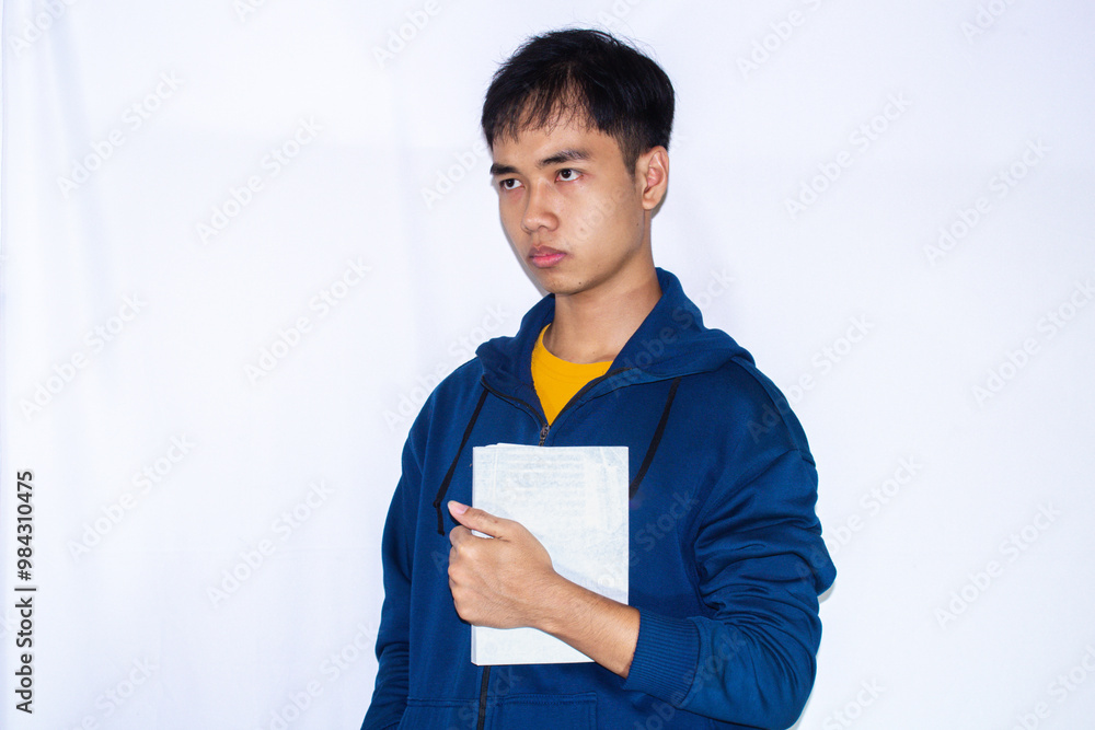 teenager wearing dark blue jacket and yellow shirt, facing right side with serious expression while holding book teenager wearing dark blue jacket and yellow shirt, facing right side with serious expression while holding book