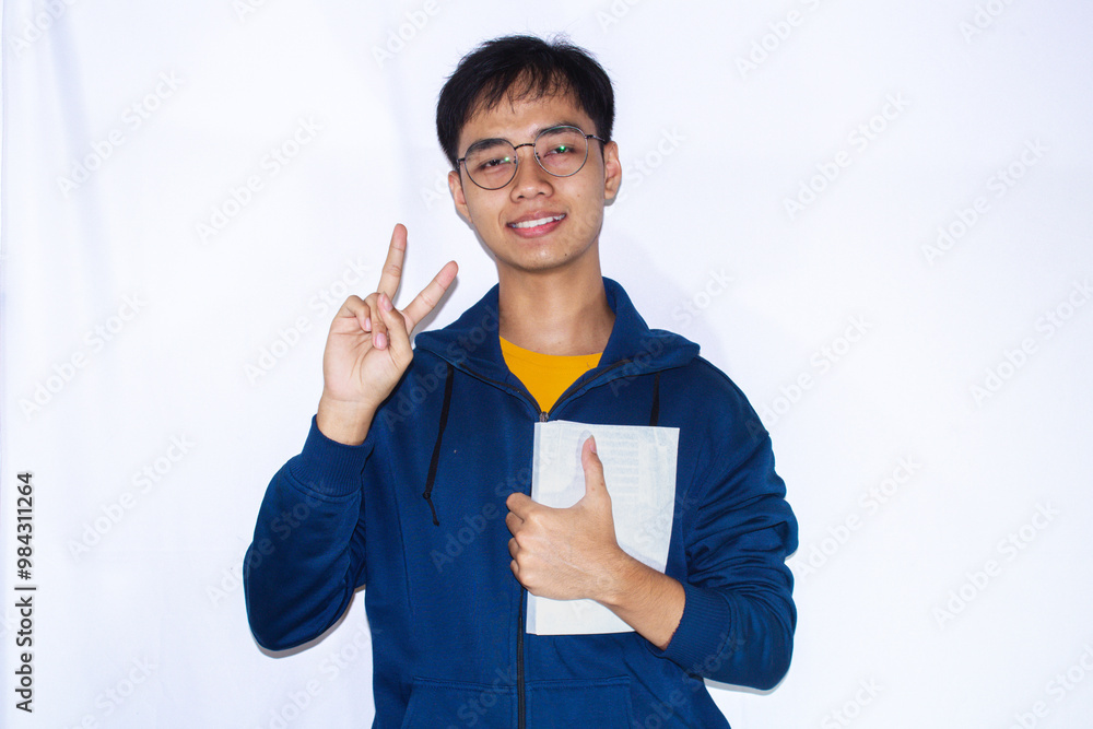 teenager wearing dark blue jacket and yellow shirt, facing forward and posing with two fingers while holding a book teenager wearing dark blue jacket and yellow shirt, facing forward and posing with two fingers while holding a book