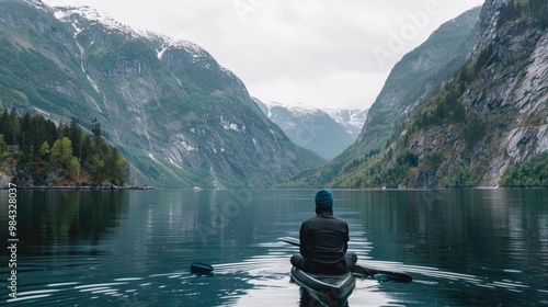 Person sitting peacefully by calm mountain lake reflecting snowy peaks and trees