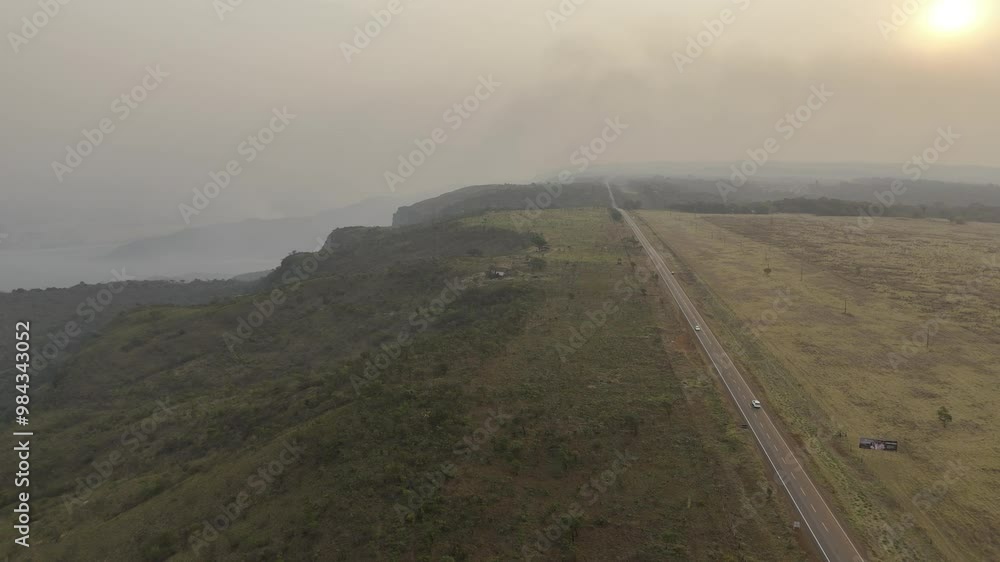 Drone flies into sunset, along highway next to valley with wildfires and smoke near Chapada Guimarães, Mato Grosso, Brazil Drone flies into sunset, along highway next to valley with wildfires and smoke near Chapada Guimarães, Mato Grosso, Brazil