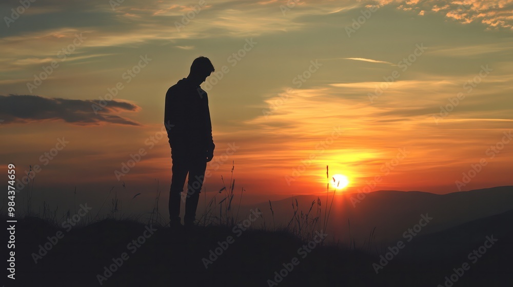 Obraz premium A silhouette of a sad man standing on a hill, with the sun setting in the background, casting a long shadow
