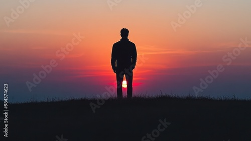 A silhouette of a sad man standing on a hill, with the sun setting in the background, casting a long shadow