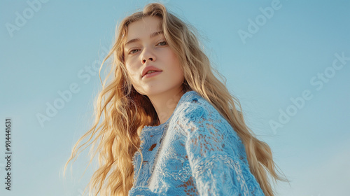 An ethereal model with white hair, wearing an oversized blue knit cardigan adorned with delicate lace details and embroidered flowers.