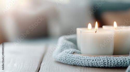 Three white candles are burning peacefully on a soft blue knit blanket, creating a warm and cozy atmosphere, perfect for relaxation and tranquility.