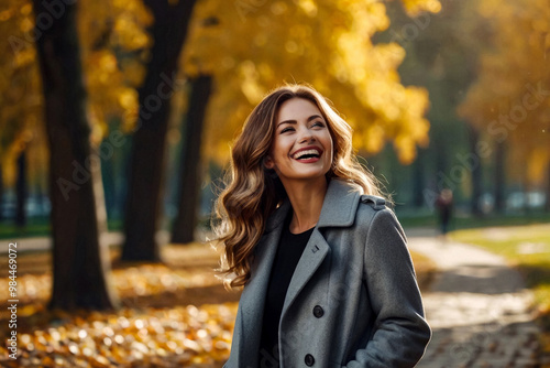 Perfect smiling lady in grey coat posing in autumn park, looking up away. Portrait of happy young woman enjoying on fresh air on September fall day. Leisure activity concept. Copy ad text space