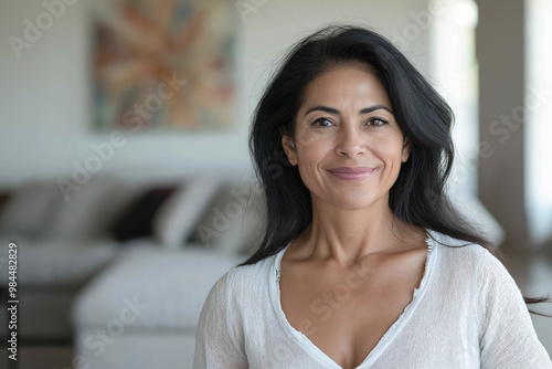 Photo of a smiling 50-year-old Hispanic woman in a light-colored sweater on the right. The woman is in the living room. Advertising banner.