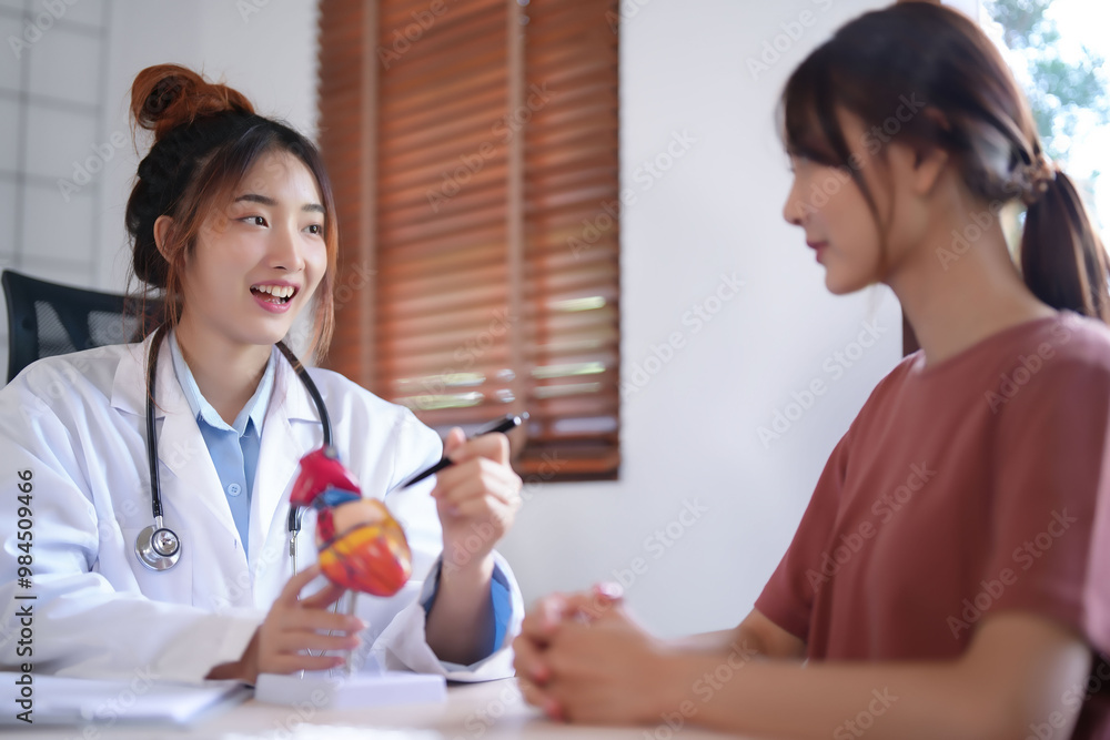 Asian cardiologist doctor women pointing on anatomical of human heart model to explaining medical data and giving counseling mental health therapy to female patient after examining health in clinic Asian cardiologist doctor women pointing on anatomical of human heart model to explaining medical data and giving counseling mental health therapy to female patient after examining health in clinic