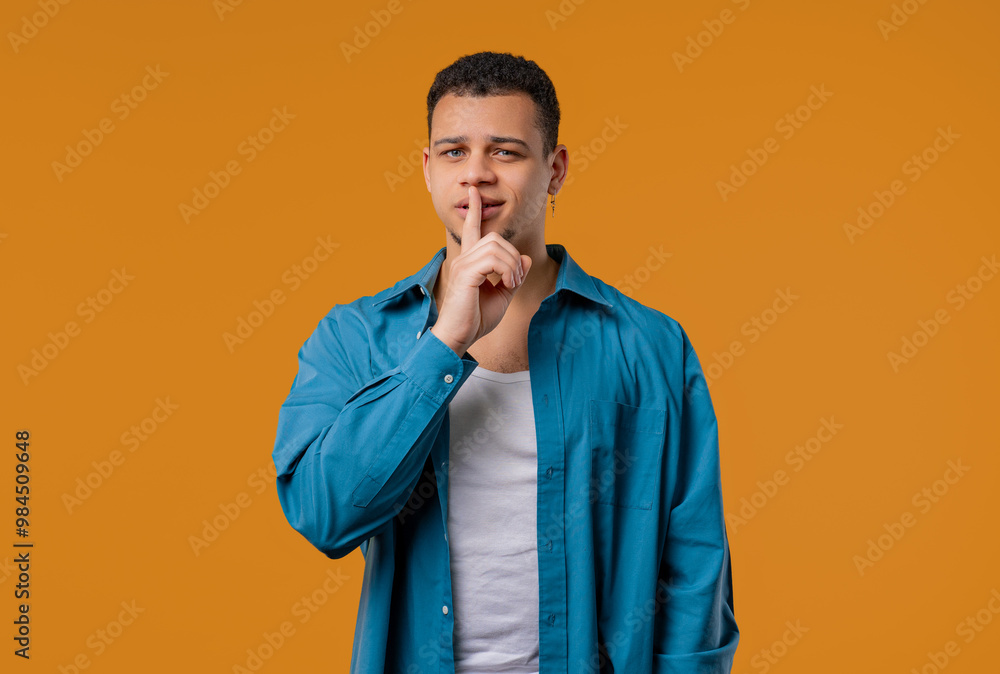 Handsome man with gesture of shh, secret, silence, conspiracy, gossip on yellow Handsome man with gesture of shh, secret, silence, conspiracy, gossip on yellow
