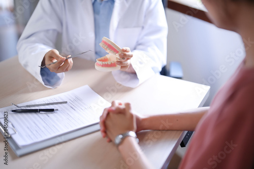 Asian dentist doctor women holding model of human jaws with teeth explaining about oral dental treatments to female patient while examination teeth and discussion about dental health in dental clinic photo