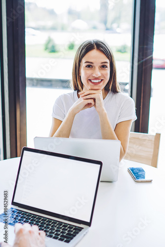 Portrait of cheerful hipster girl sitting at table with laptop device with cute smile on face, young man searching information via modern computer with blank screen area for your internet advertising