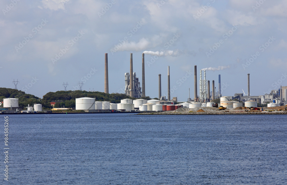 Wide modern cement factory with high chimneys puffing out white smoke and the seaside during the production of cement Wide modern cement factory with high chimneys puffing out white smoke and the seaside during the production of cement