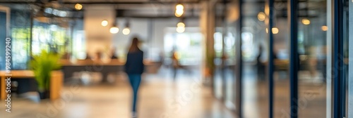 Blurred silhouette of person walking in modern office hallway with glass walls, warm lighting, and sleek design, creating an atmosphere of professionalism and innovation.