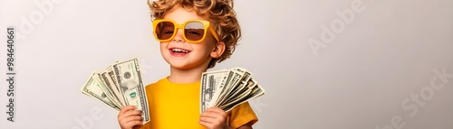 A cheerful child wearing sunglasses and an orange shirt, proudly holding stacks of cash, exuding a playful, money-related vibe.