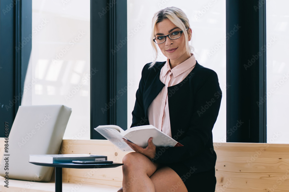 Portrait of successful female entrepreneur in elegant wear looking at camera during time for reading in workspace, attractive caucasian woman with useful literature book in hand sitting in office Portrait of successful female entrepreneur in elegant wear looking at camera during time for reading in workspace, attractive caucasian woman with useful literature book in hand sitting in office