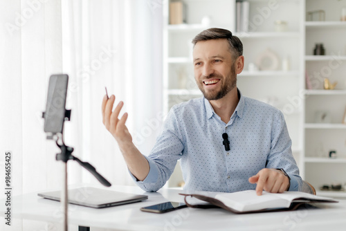 Engaging male teacher conducting an online class while seated at a desk with a laptop and notes in a bright workspace. High quality photo photo