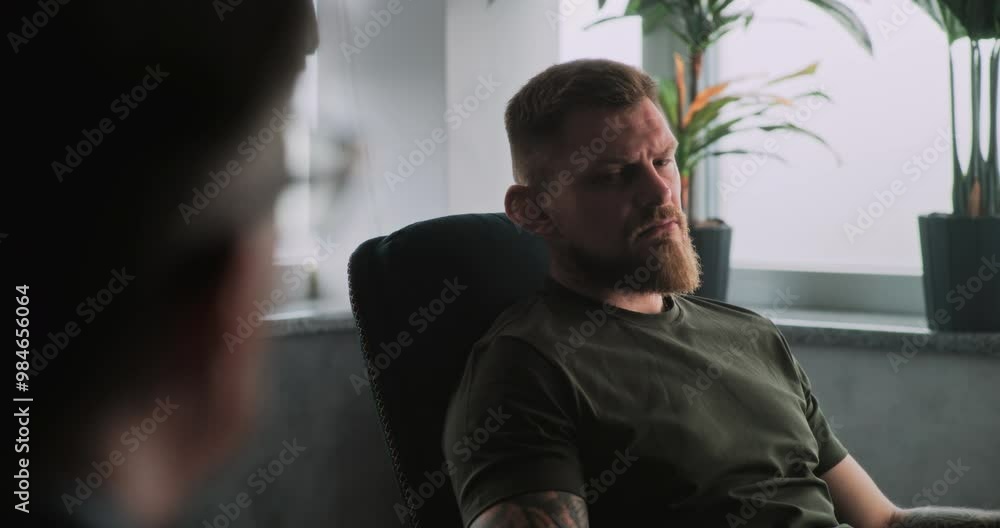 Unhappy military man with post traumatic stress disorder sits in chair, shares feelings and communicates with psychotherapist or psychologist on rehabilitation therapy session. PTSD. Over the shoulder Unhappy military man with post traumatic stress disorder sits in chair, shares feelings and communicates with psychotherapist or psychologist on rehabilitation therapy session. PTSD. Over the shoulder