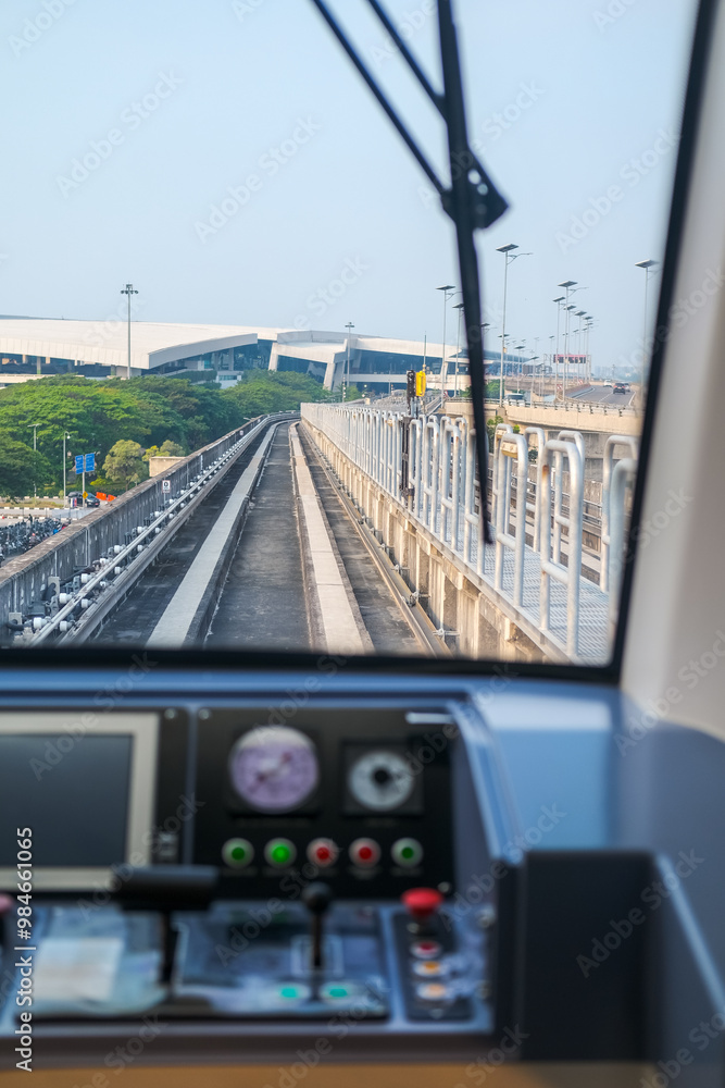 View from inside airport train shows tracks curving ahead through a tunnel, with control panel in foreground, capturing the smooth journey and modern transit experience.