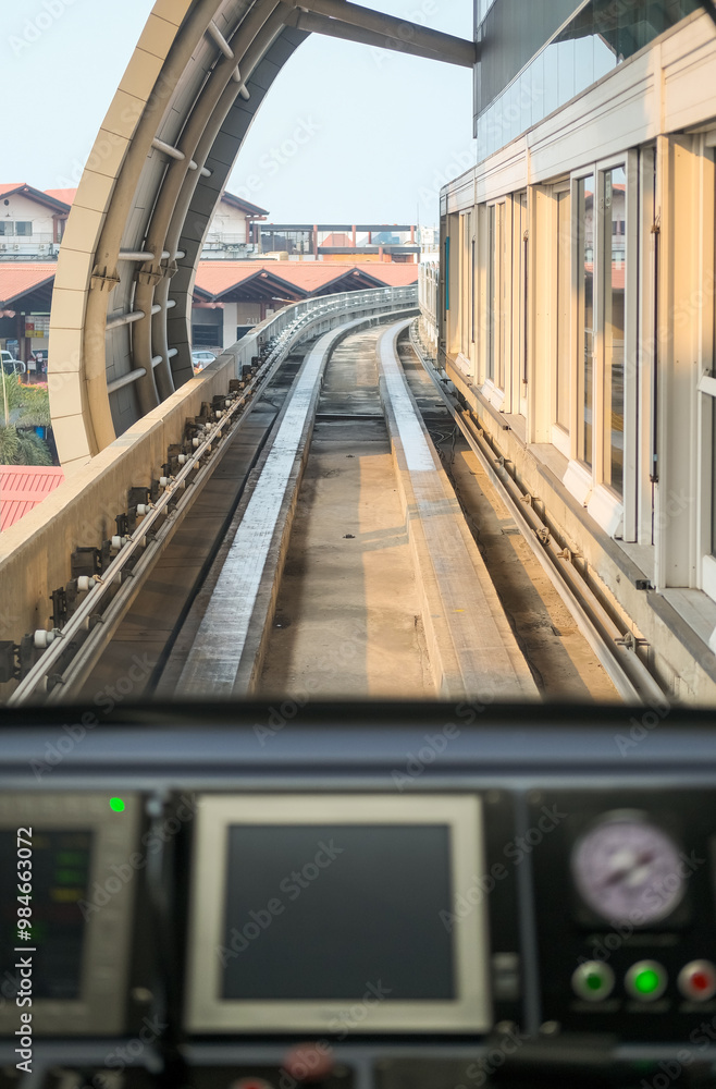 View from inside airport train shows tracks curving ahead through a tunnel, with control panel in foreground, capturing the smooth journey and modern transit experience.