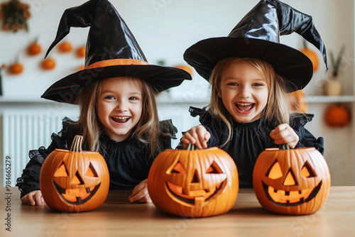 Little children in black witch costumes make jack-o'-lanterns for Halloween on the table