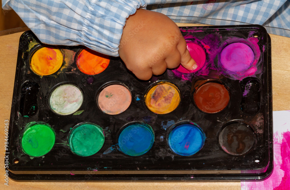 Naklejka premium a child's finger picking up finger paint from a watercolor palette