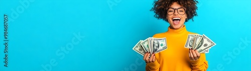 A smiling person in a yellow shirt holds stacks of cash against a bright blue background, expressing excitement and joy.