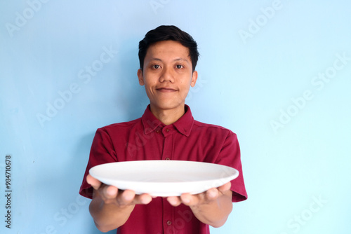 Young asian man smiling while showing empty eating plate photo