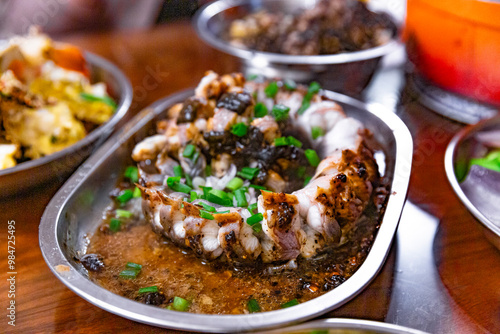 Steamed eel with black bean sauce topped with fresh scallions, served in a metal dish, showcasing the tender eel and savory sauce