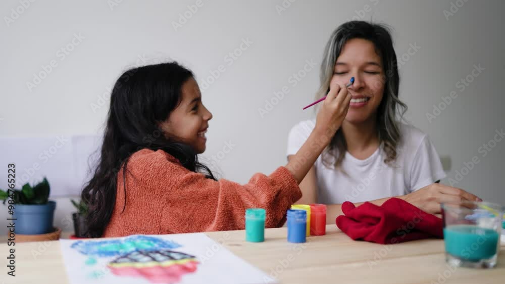 Mother and daughter having fun painting each other face at home. Happy latin family, mom and kid doing art project Mother and daughter having fun painting each other face at home. Happy latin family, mom and kid doing art project