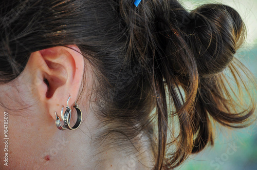 Tableau sur toile Woman's ear with multiple earrings, brown hair in messy bun, casual elegance