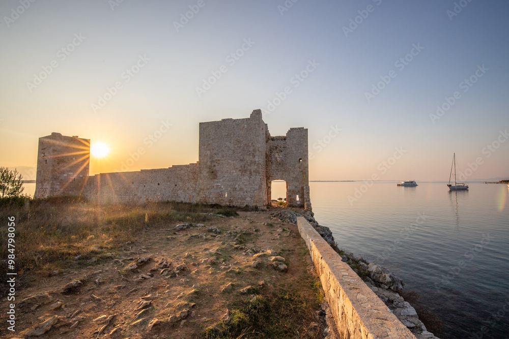 Sunrise on a Rocky Coast. Reflection in calm water. Landscape shot of the restored remains of the Venetian fortress Kastelina Castle on the Mediterranean Sea, Vir, Dalmatia, Croatia, Adriatic Sea Sunrise on a Rocky Coast. Reflection in calm water. Landscape shot of the restored remains of the Venetian fortress Kastelina Castle on the Mediterranean Sea, Vir, Dalmatia, Croatia, Adriatic Sea
