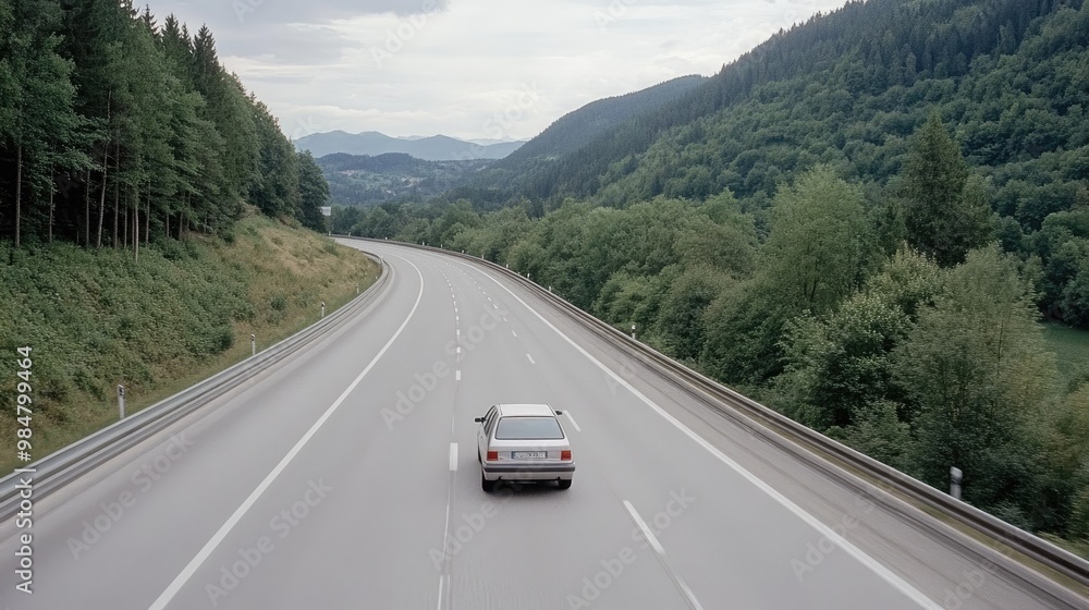 Naklejka premium A solitary silver SUV travels the wide motorway in Germany, surrounded by gray asphalt and soft lighting from the overcast sky, creating a tranquil ambiance