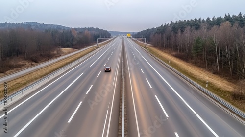 A solitary silver SUV travels the wide motorway in Germany, surrounded by gray asphalt and soft lighting from the overcast sky, creating a tranquil ambiance