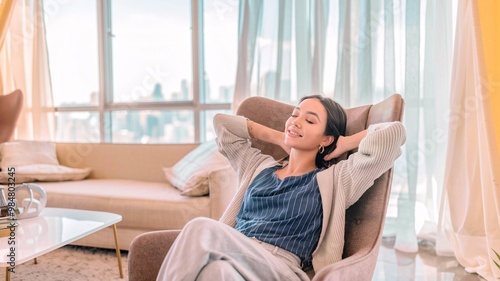  Relaxed Young Woman in Cozy Chair by Window, Enjoying Peaceful Moment. This image evokes feelings of peace, comfort, and home.