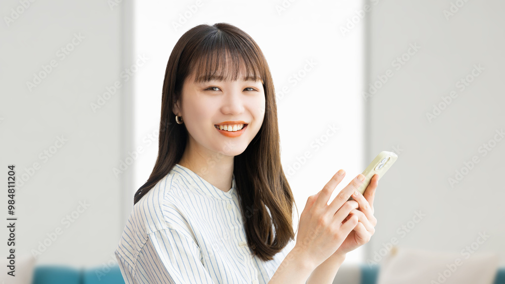 リビングでスマホを持つ笑顔の女性 リビングでスマホを持つ笑顔の女性