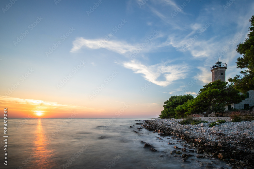 Beautiful sunset in a landscape on a rocky coast with a striking lighthouse and pine forest. View over the coast to the building, on the Mediterranean, Vir, Dalmazien, Croatia, Adriatic Beautiful sunset in a landscape on a rocky coast with a striking lighthouse and pine forest. View over the coast to the building, on the Mediterranean, Vir, Dalmazien, Croatia, Adriatic