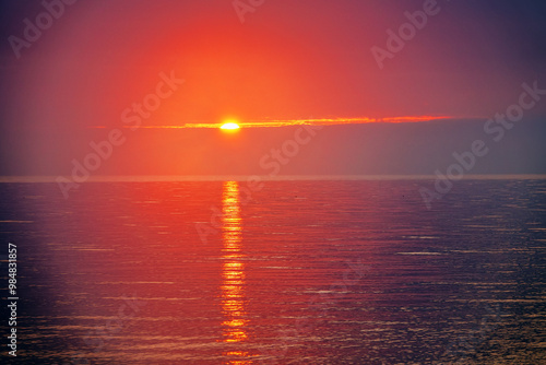 Sunny path, sun glade, road to luminary. Low winter position of evening sun over calm lake, Ripples of water are colored in red-gold tones. Halo around sun is like lighthouse lantern photo