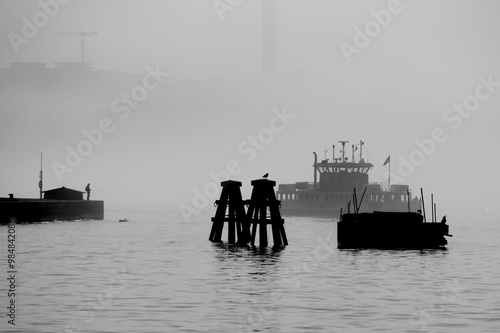 Black and white picture, passenger ferries in the bay Strömmen a foggy morning, dolphin and rod fishing on a pier. A sunny summer day in Stockholm photo