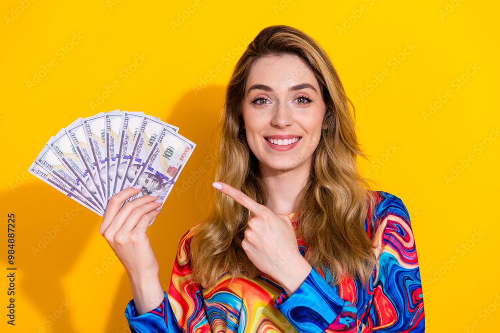 Photo portrait of pretty young girl point hold money fan wear trendy colorful outfit isolated on yellow color background Photo portrait of pretty young girl point hold money fan wear trendy colorful outfit isolated on yellow color background