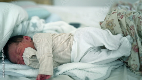 Newborn baby crying in bed, swaddled in a blanket, clearly in distress. a raw and emotional moment, highlighting the vulnerability and intensity of early life in a home environment photo