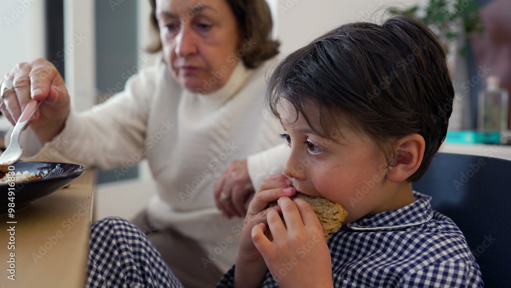 Young boy opens wide to be fed by grandmother, capturing the moment of trust and care during a meal at home. Strong bond between grandparent and child in a comfortable, loving environment Young boy opens wide to be fed by grandmother, capturing the moment of trust and care during a meal at home. Strong bond between grandparent and child in a comfortable, loving environment